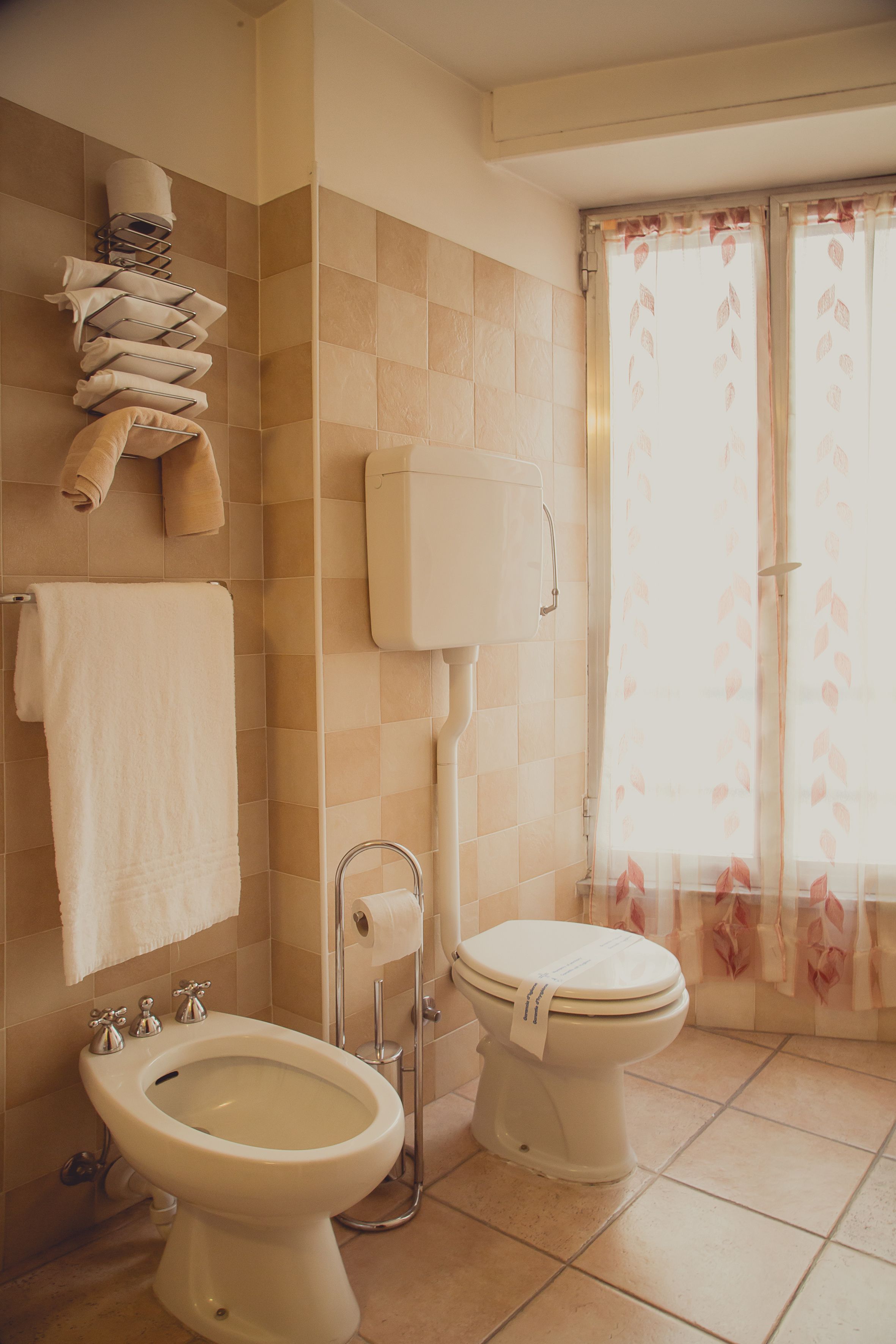Een badkamer met een hygiëneschuimer, toilet en een handdoekrek met handdoeken.
