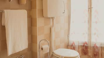 Een badkamer met een hygiëneschuimer, toilet en een handdoekrek met handdoeken.