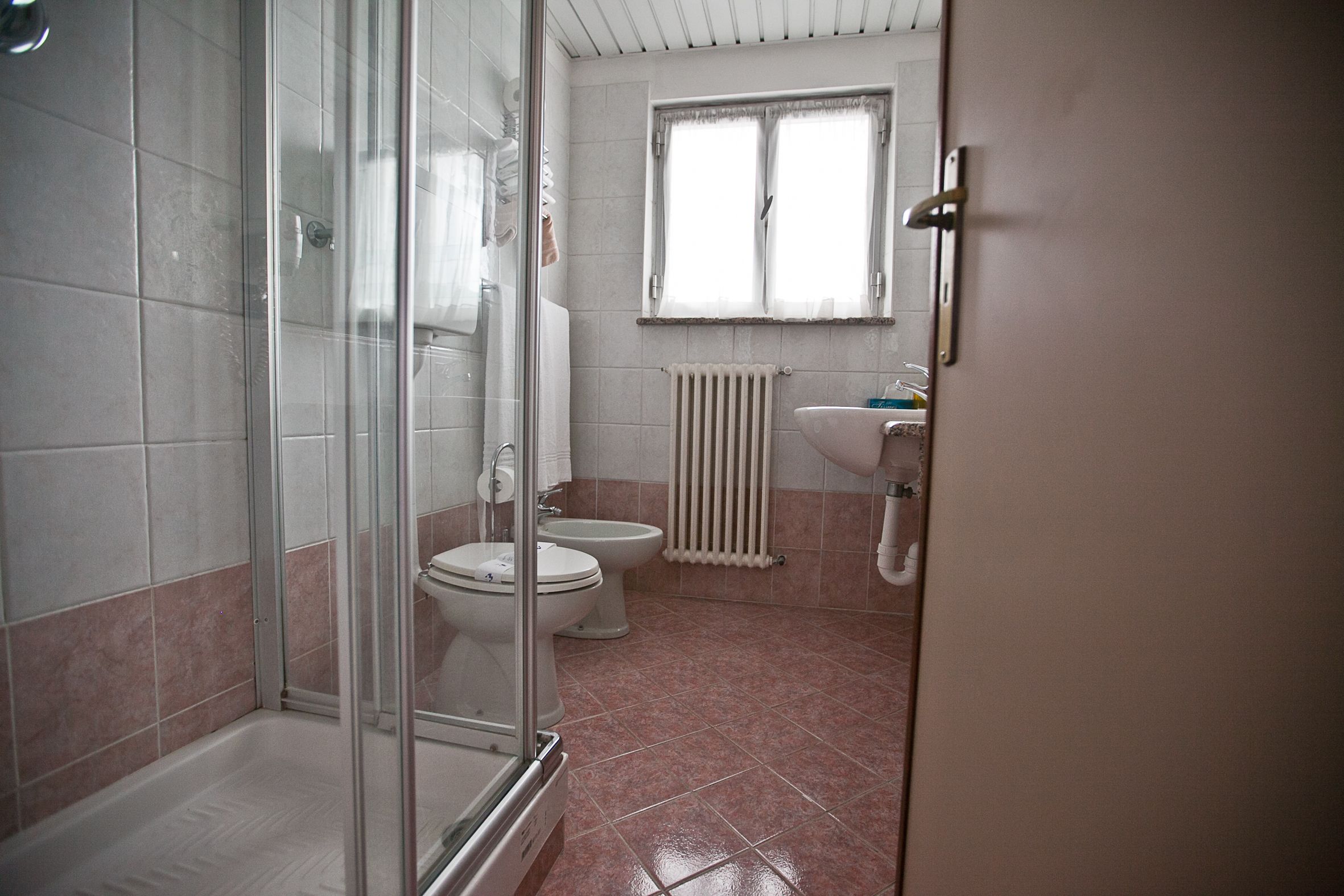Un bagno con doccia vetrata, due servizi igienici, un lavandino e una finestra.