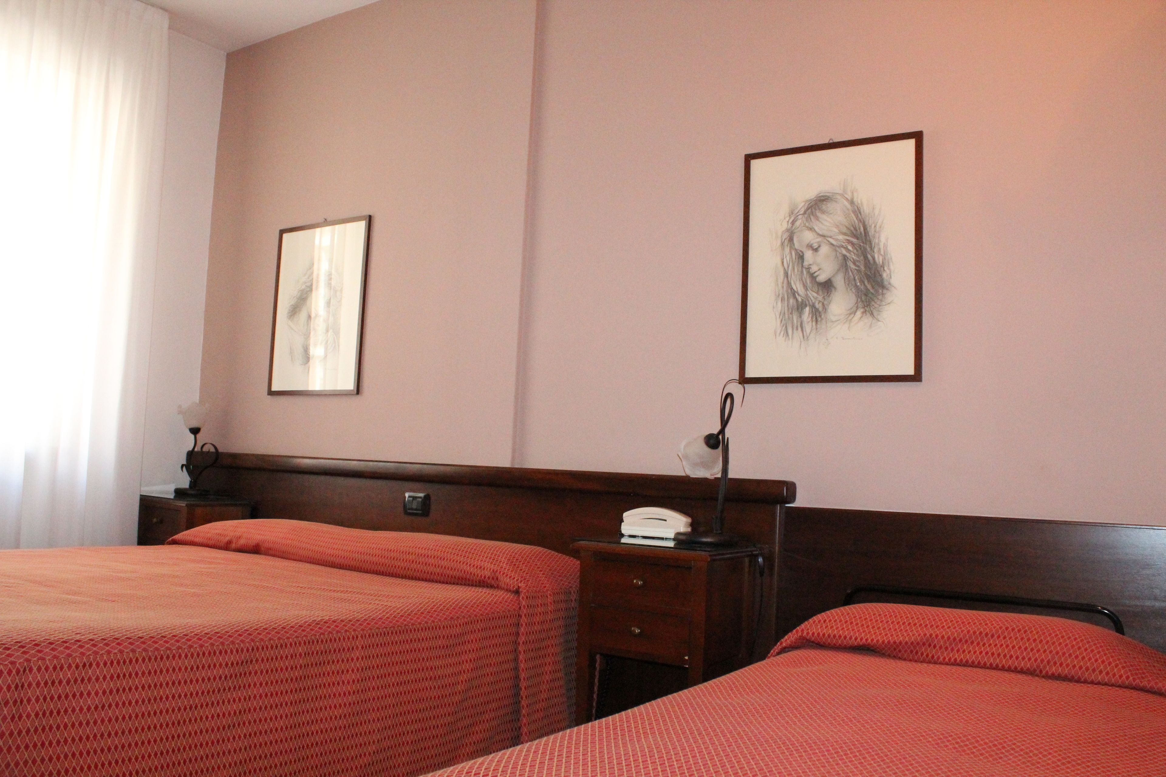 Habitación de hotel con dos camas, una mesita de noche con lámpara y dos cuadros en la pared.