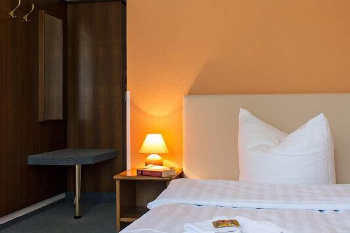 Una habitación de hotel con cama, una mesita de noche con lámpara, un armario de madera y una pequeña mesa.