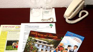 A desk with a telephone, a brochure titled "LAND HOTEL ALT-JOCKETA," a menu, and a glass with a bottle.