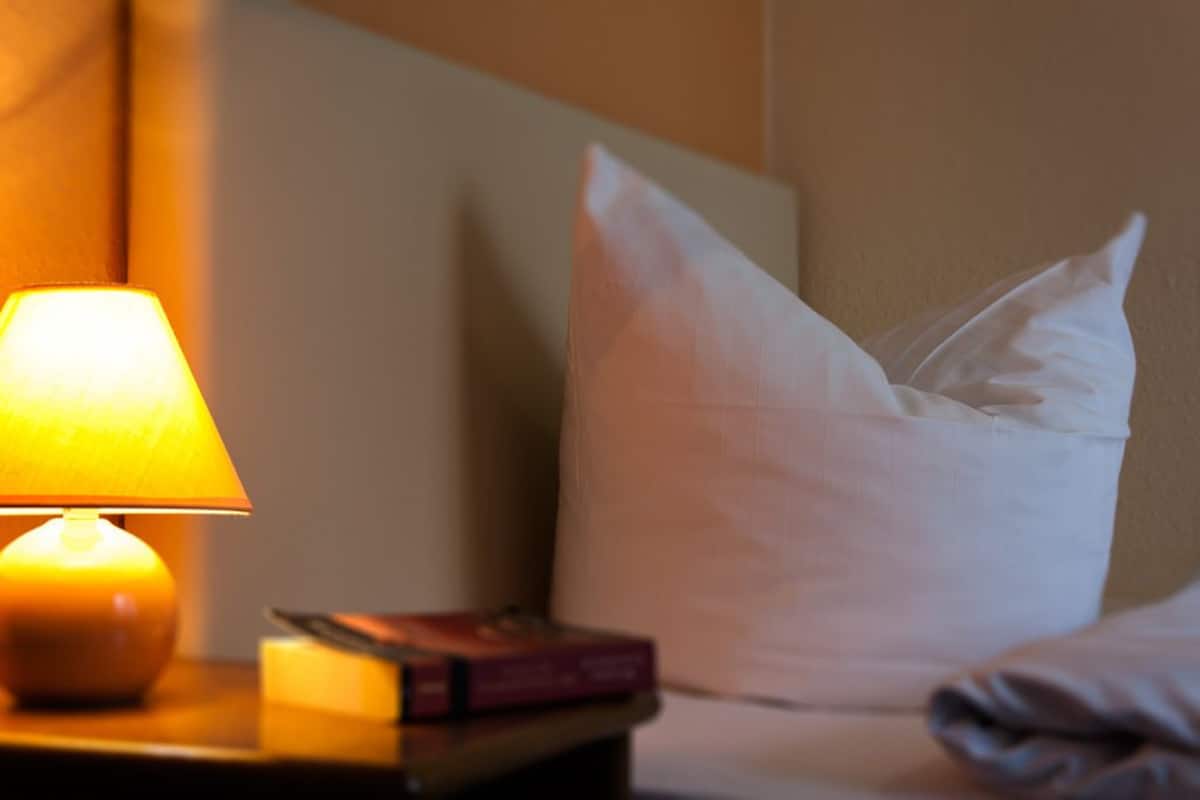 Una mesita de noche con una lámpara, un almohadón y un libro.