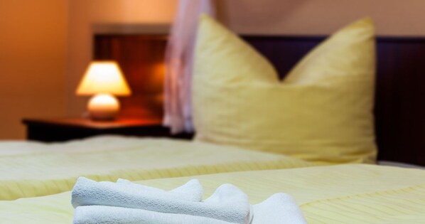 Una cama bien hecha con un cabecero amarillo y almohadas, una lámpara de noche y una mesita de noche a la vista.