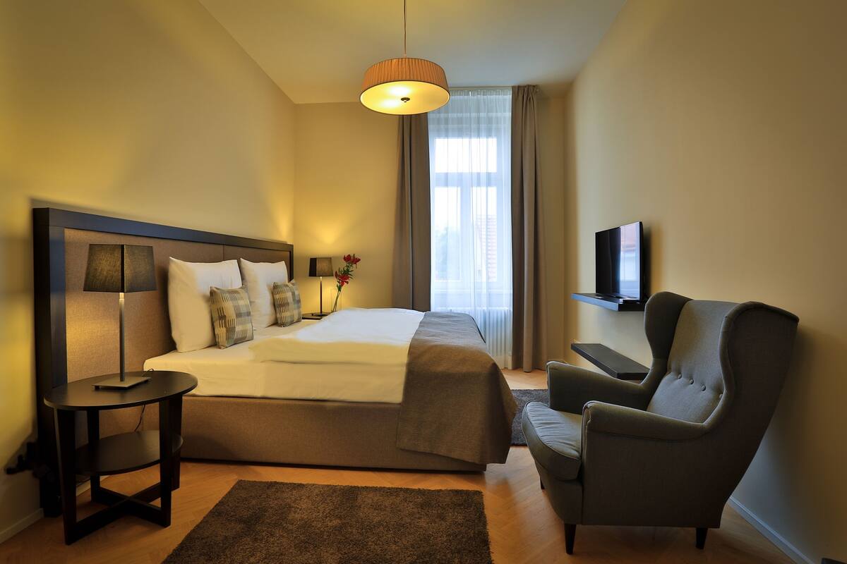 A hotel room with a bed, a chair, a TV, and a lamp.