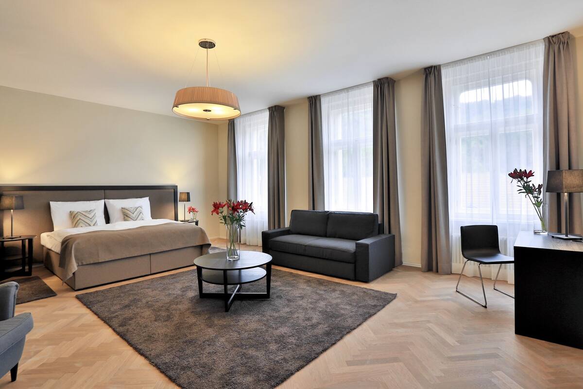 A modern hotel room with a bed, sofa, coffee table, and a desk.
