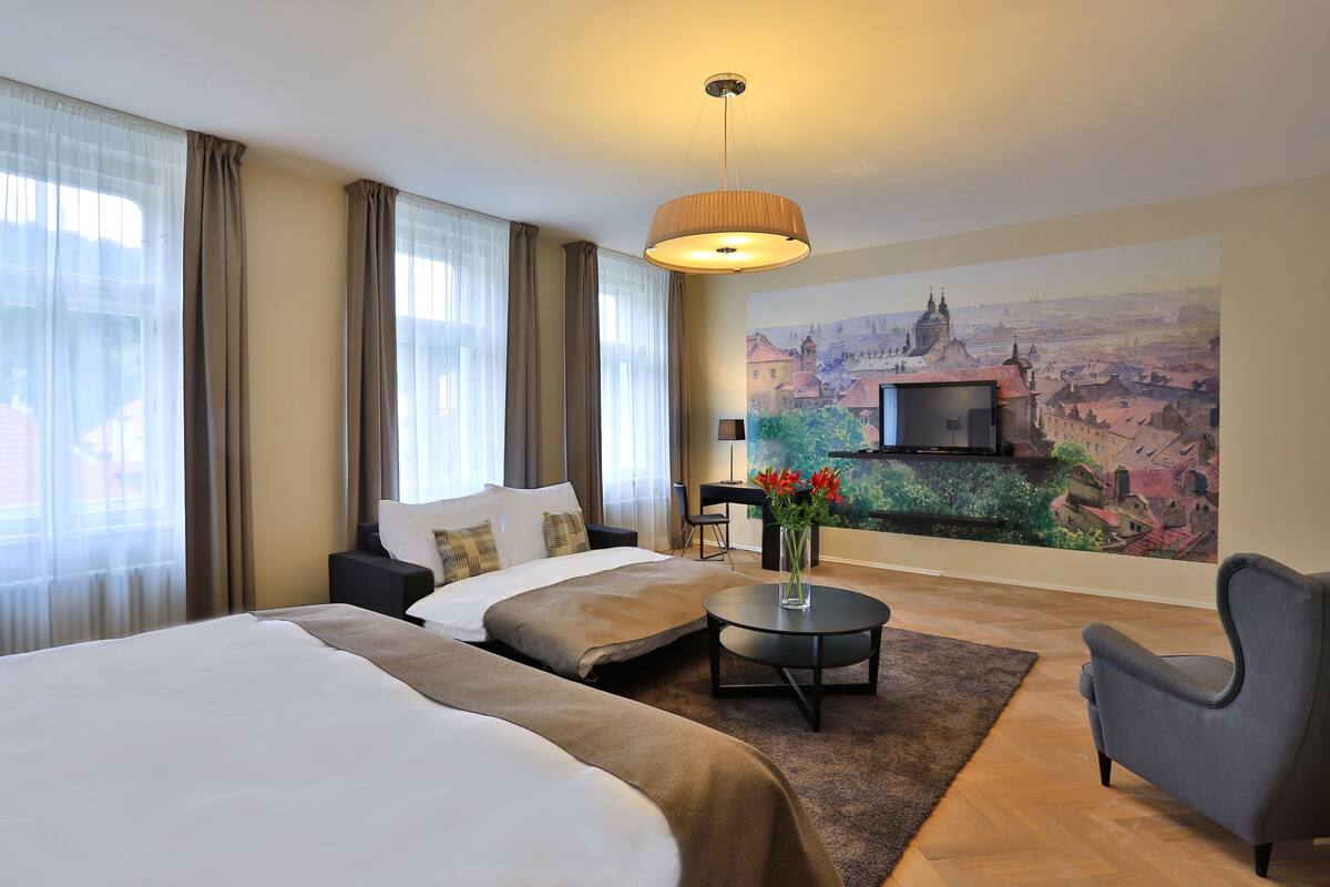 A hotel room with two beds, a sofa, a desk, a TV, and a mural of a cityscape.