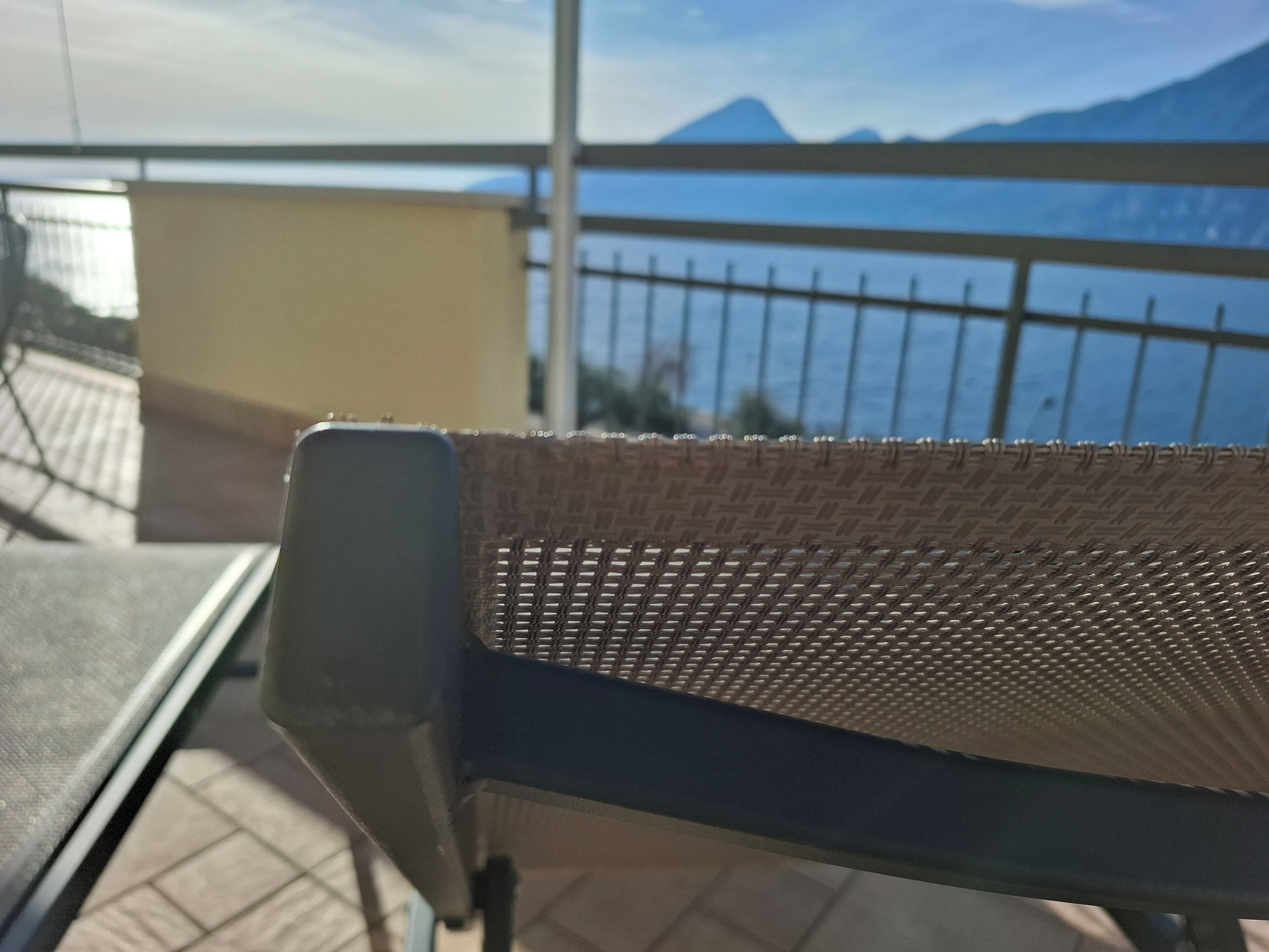 Een stoel met een gevlochten rugleuning, een metalen tafel en uitzicht op een waterpartij met bergen op de achtergrond.