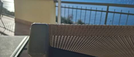 Een stoel met een gevlochten rugleuning, een metalen tafel en uitzicht op een waterpartij met bergen op de achtergrond.