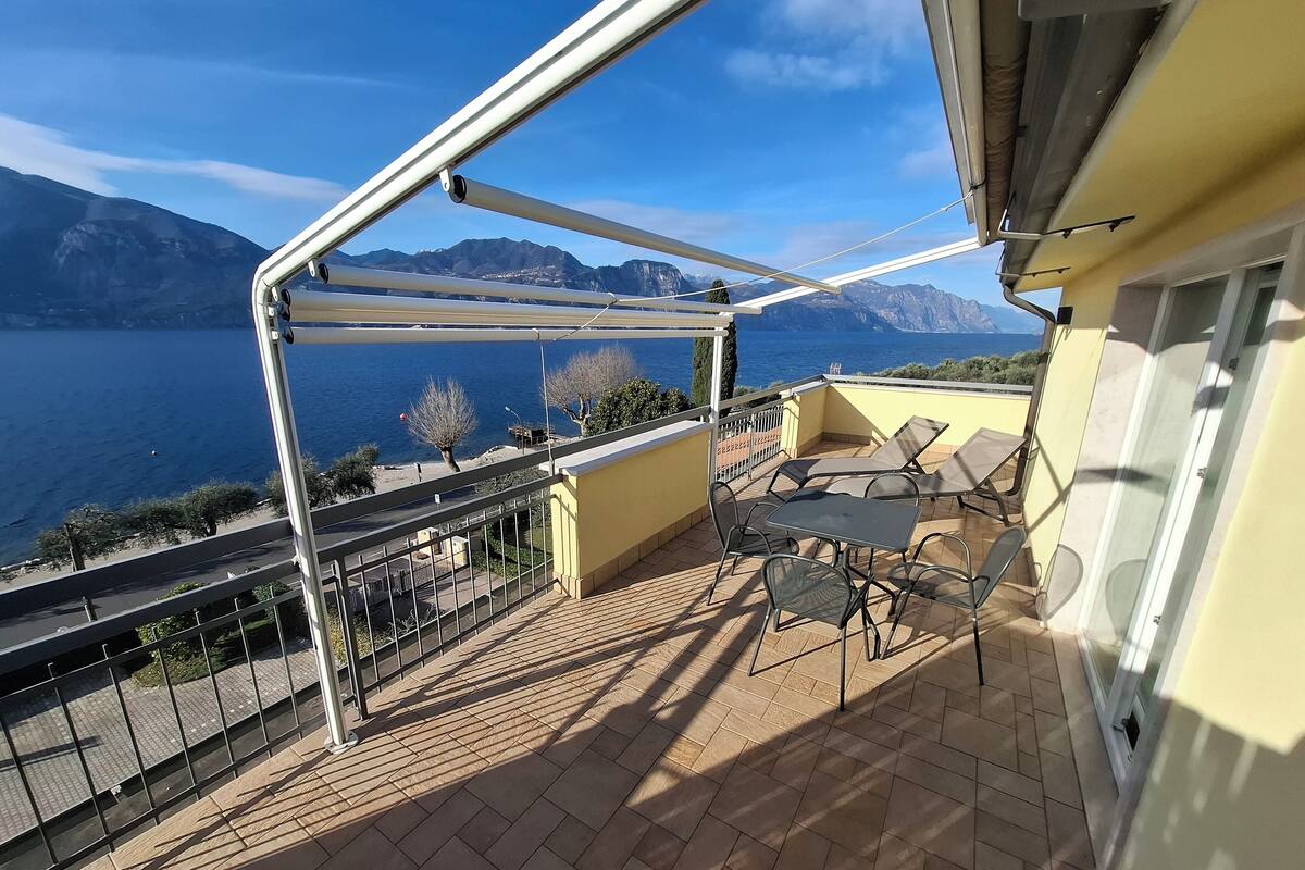 A balcony with a view of the sea and mountains, furnished with a table and chairs.