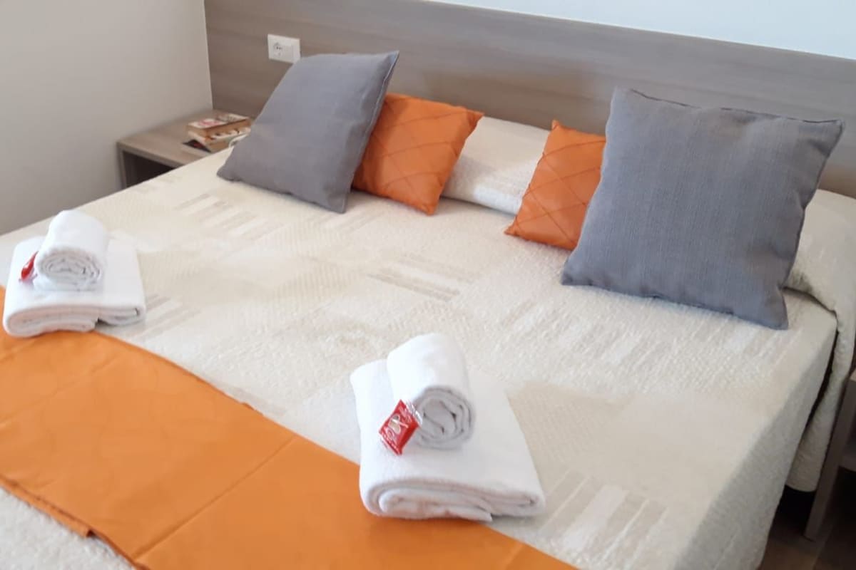 Una cama bien hecha con un edredón blanco, dos toallas dobladas y una variedad de almohadas en diferentes colores.