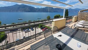 A balcony with a view of a lake and mountains. There are lounge chairs and a table with a cup on it. - Casa Alkea (Brenzone sul Garda)
