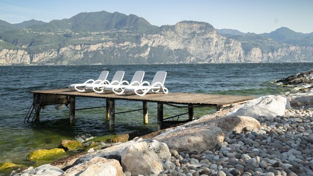 A wooden pier with white lounge chairs extending over a rocky shoreline. - Casa Alkea (Brenzone sul Garda)