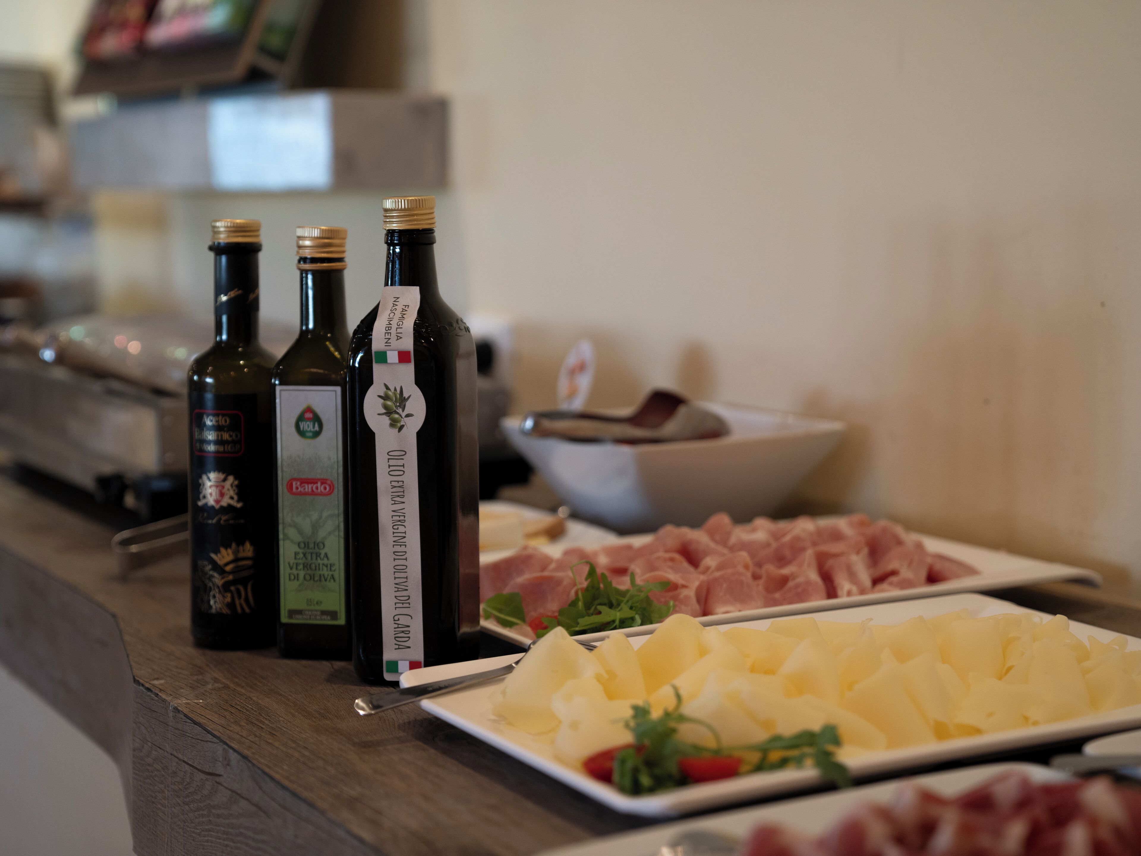 Ein Tisch mit drei Olivenölflaschen, einer Käseplatte und einer Schüssel mit Wurstwaren.