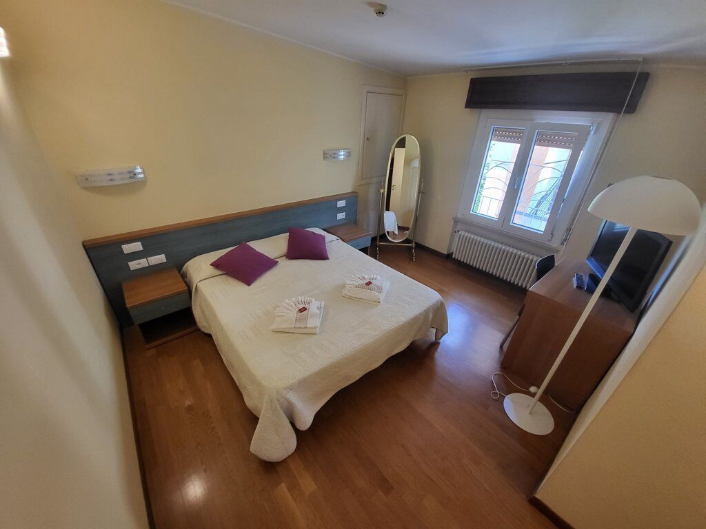 Ett hotellrum med en säng, ett nattduksbord, en spegel, ett fönster, ett element och en lampa.