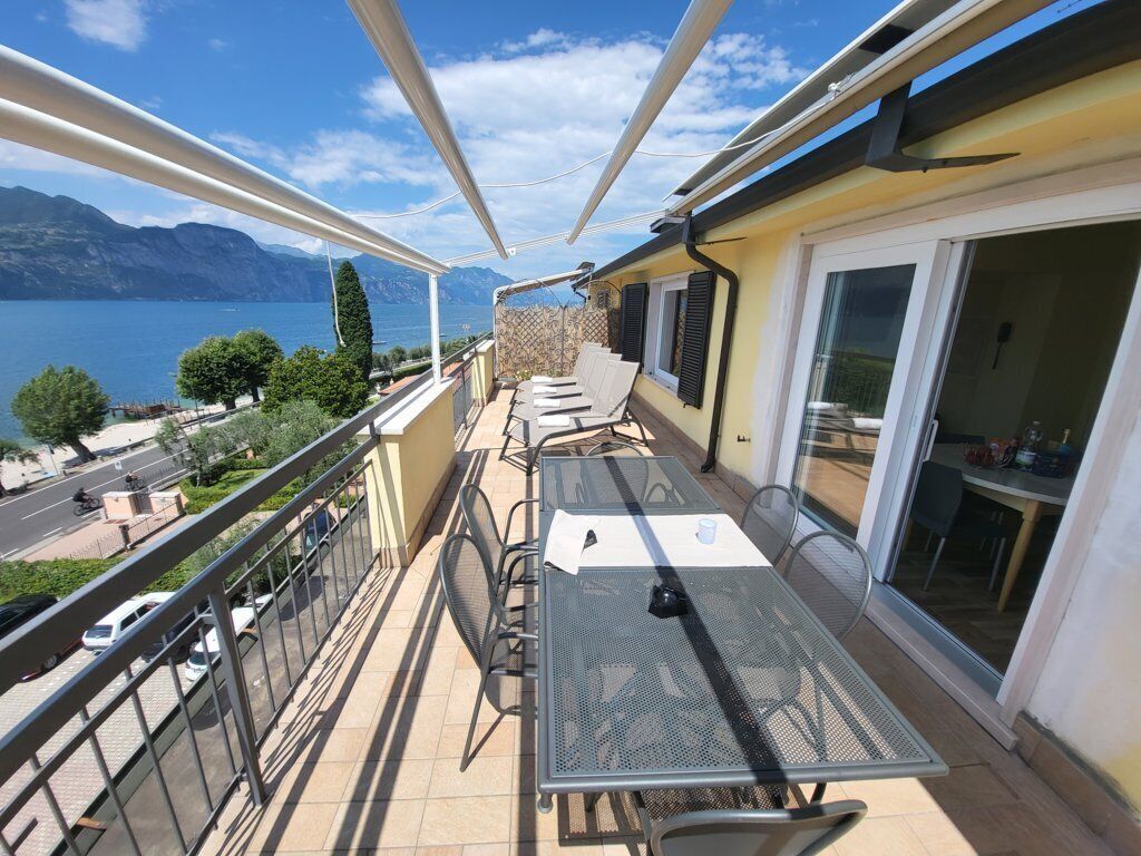 A balcony with a table and chairs, overlooking a lake and mountains.