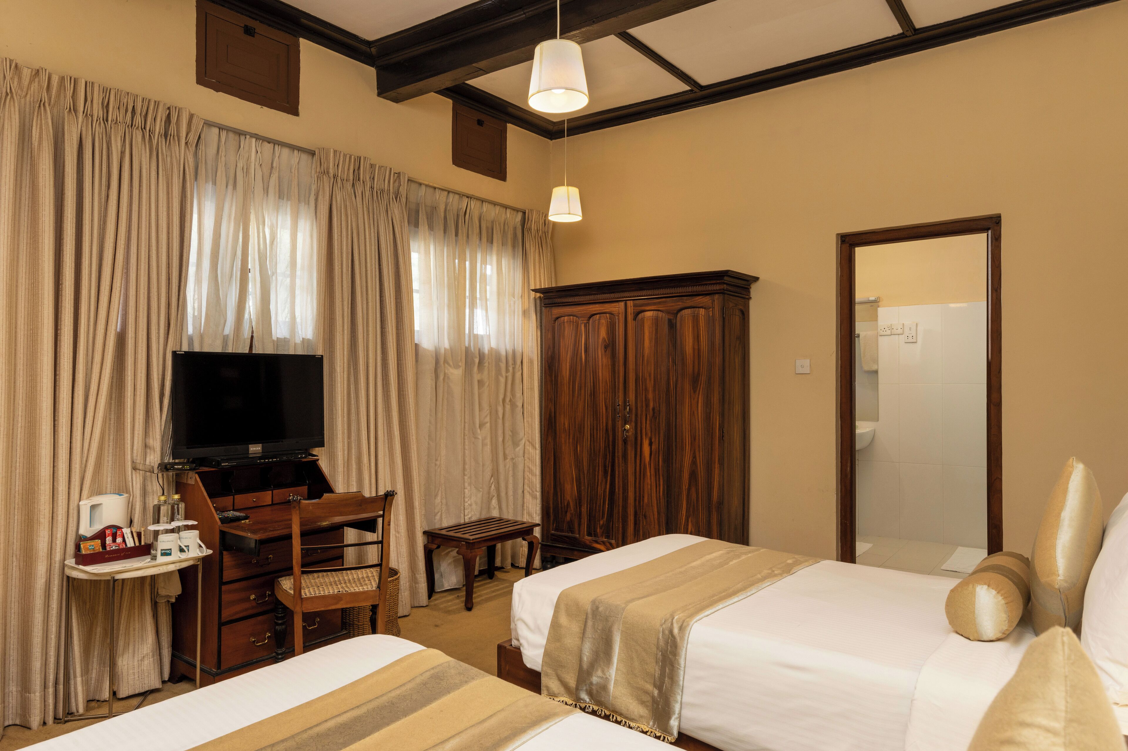 A hotel room with two beds, a television, a wooden wardrobe, and a desk with a chair.