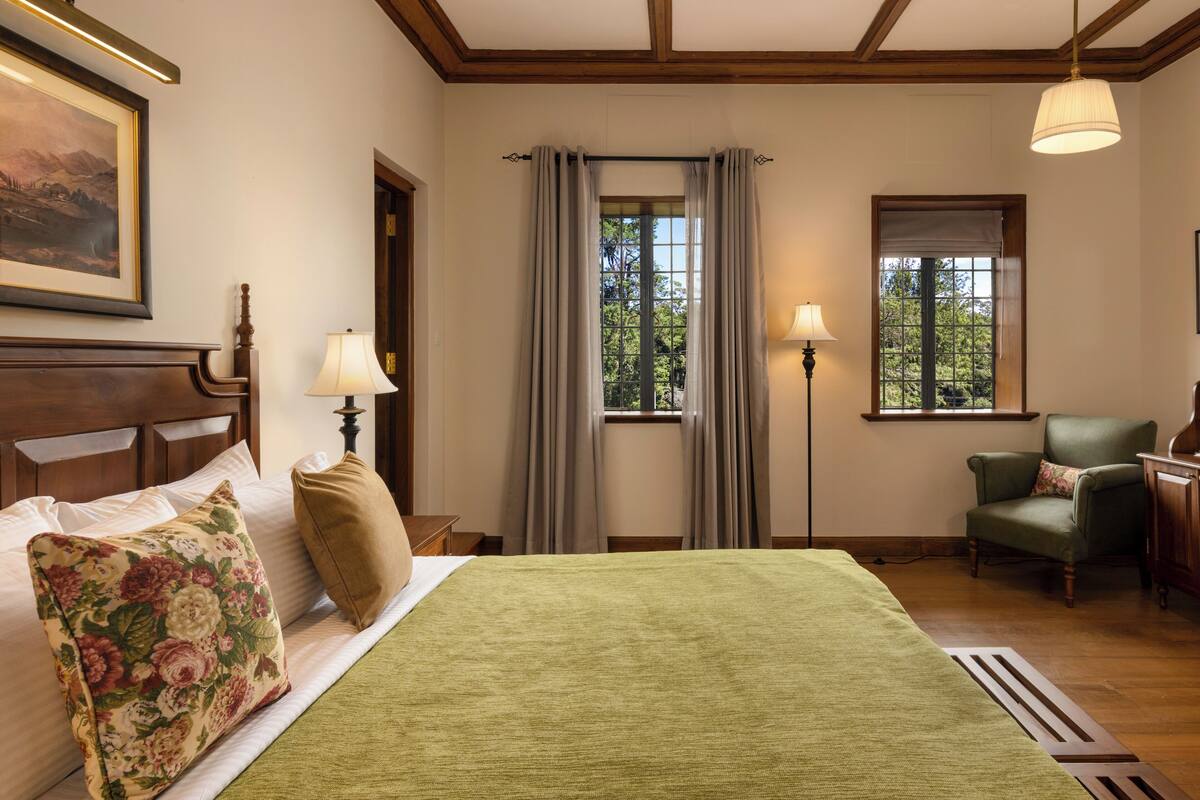 Un dormitorio ordenado con una cama grande, dos lámparas de noche, una silla y una ventana con cortinas.