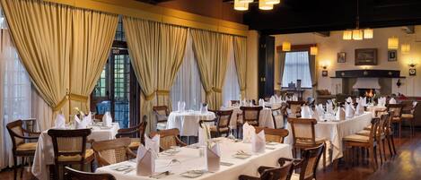 A restaurant with long tables set for dining, wooden chairs, and chandeliers.