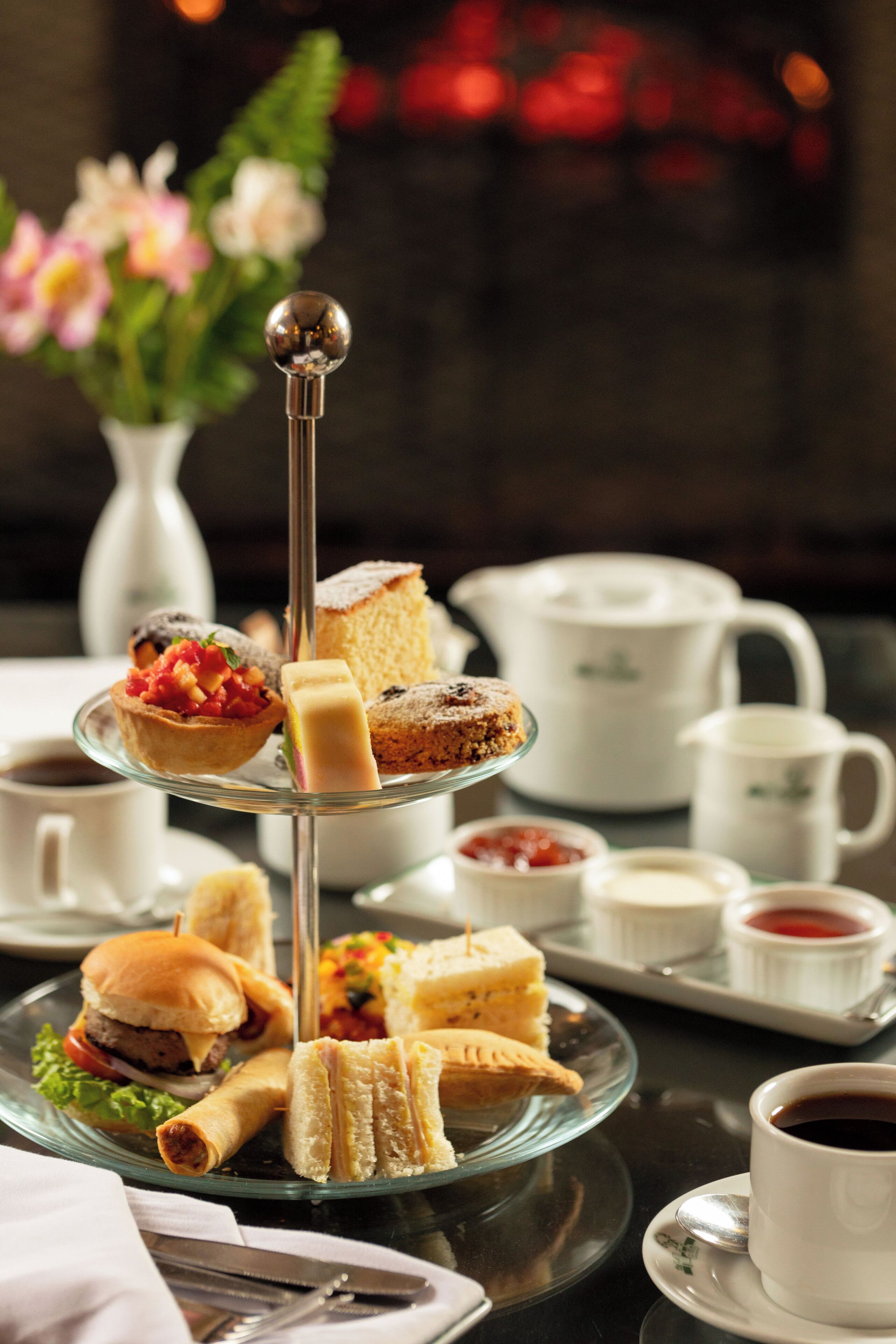 A tiered serving tray with sandwiches, pastries, and a cup of coffee.