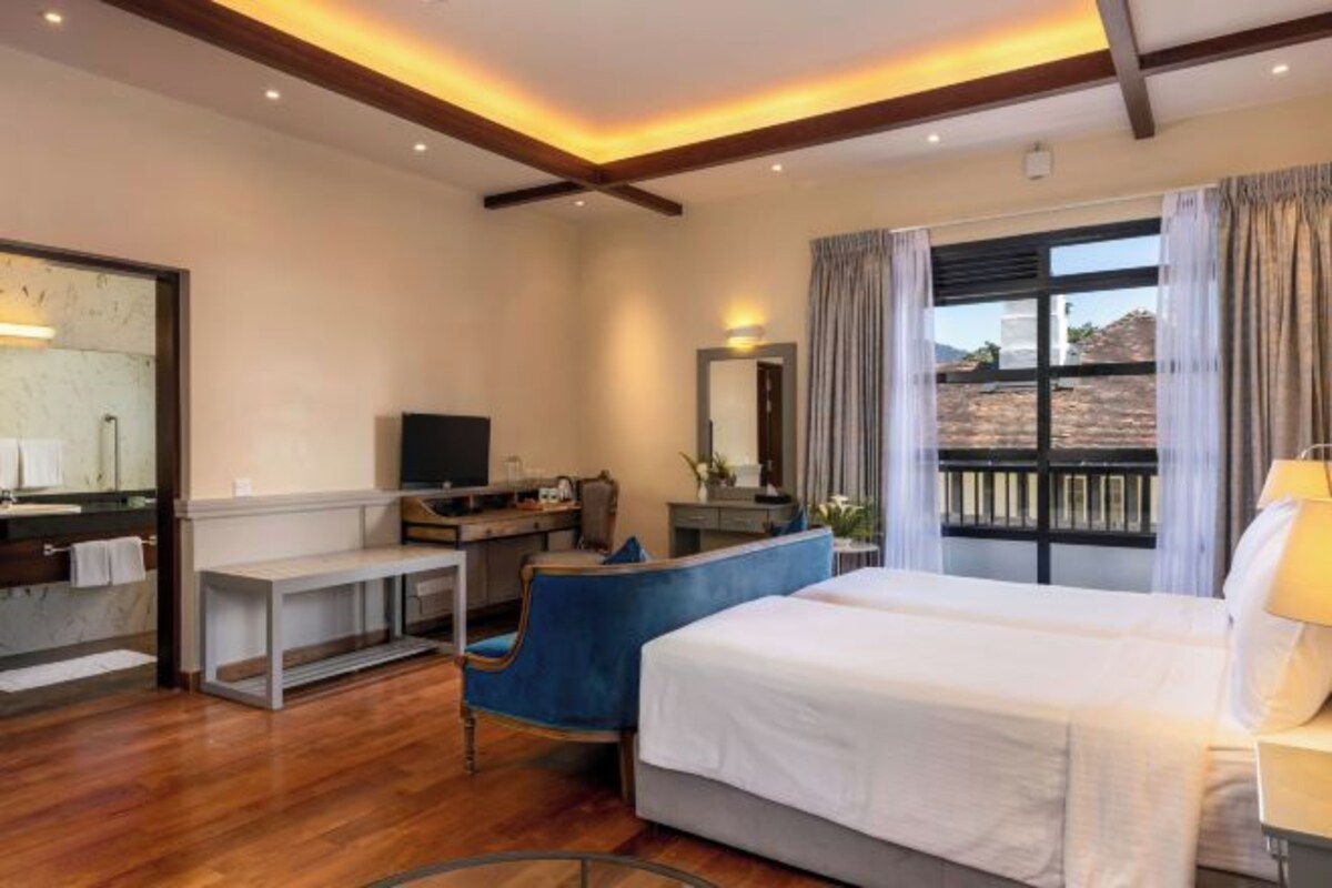 A hotel room with a bed, a desk, a chair, a TV, and a large window with curtains.