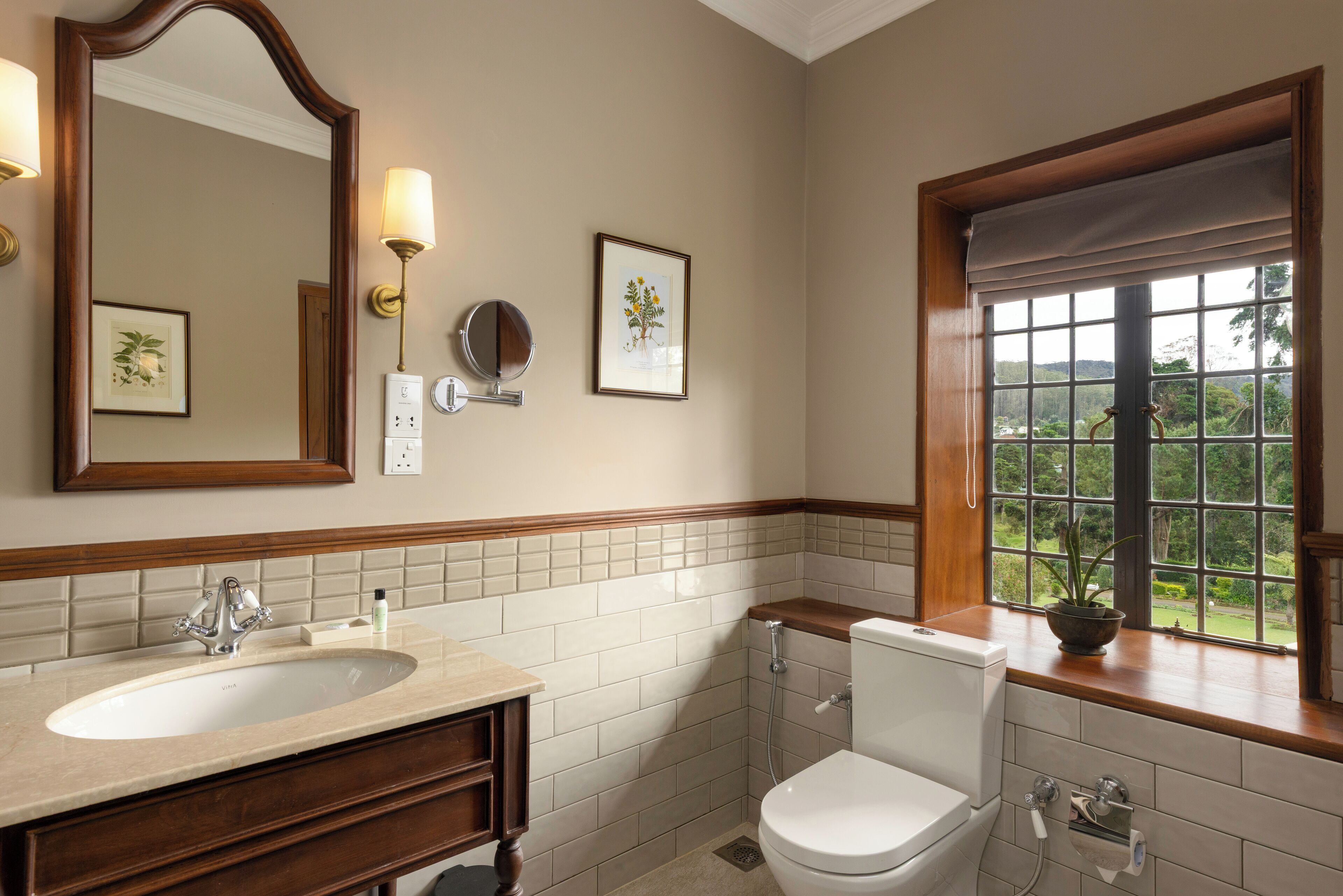 Une salle de bain équipée d’un lavabo, d’un miroir, de toilettes et d’une fenêtre donnant sur un paysage agréable.