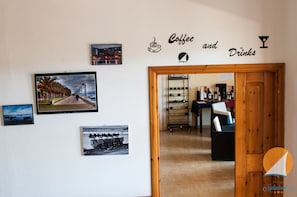 Eine Wand mit verschiedenen gerahmten Fotografien, ein Schild mit der Aufschrift 'Coffee and Drinks' und eine Holztür, die zu einem Raum mit Barbereich führt.