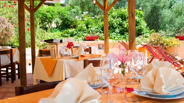 Een terras met eettafels voor twee personen, voorzien van keurig gevouwen servetten, wijnglazen en een champagnefles.