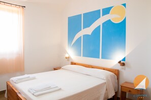 Ein Hotelzimmer mit Bett, Nachttisch, Wandbild und einem Fenster mit Vorhängen.