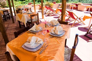 An outdoor dining area with tables set for two, chairs, and a garden view. - Hotel Maladroxia (Sant'Antioco)