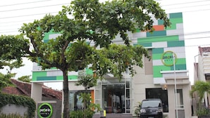 A hotel with a modern facade, a prominent green logo, and a car parked in front.