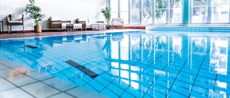 An indoor swimming pool with clear blue water, surrounded by wicker furniture and potted plants.