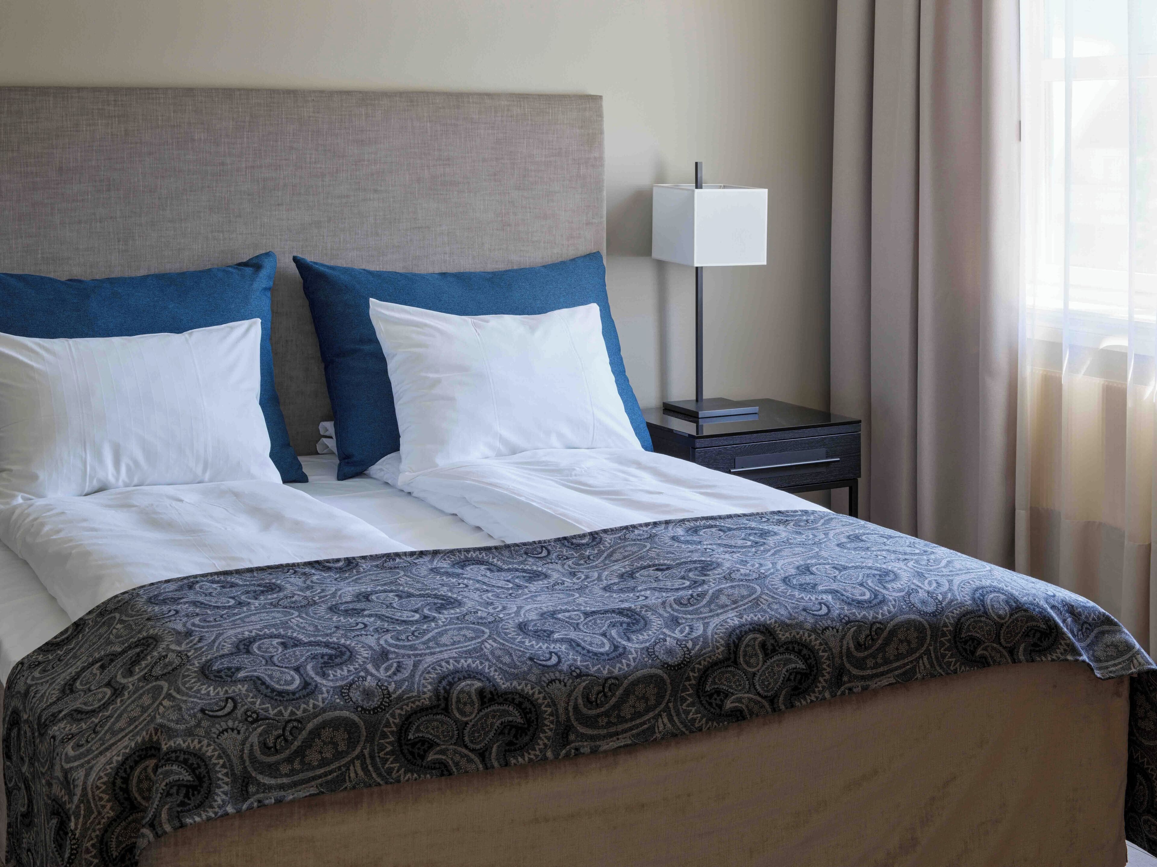 A neatly made bed with a patterned bedspread, a headboard, and a bedside table with a lamp.