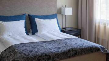 A neatly made bed with a patterned bedspread, a headboard, and a bedside table with a lamp.