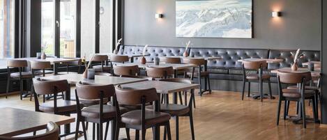 Un interior de restaurante moderno con mesas y sillas de madera, una amplia zona de asientos con bancos acolchados y un cuadro grande en la pared.