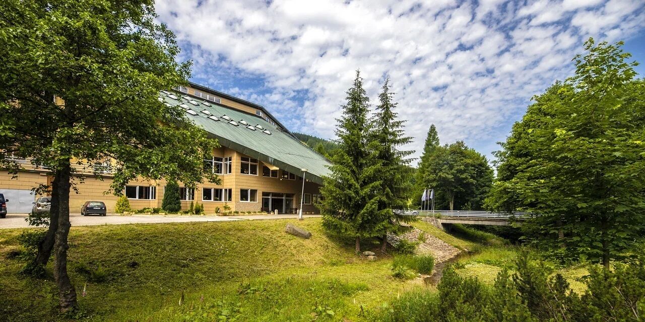 A building with a green roof, surrounded by trees and a grassy area.