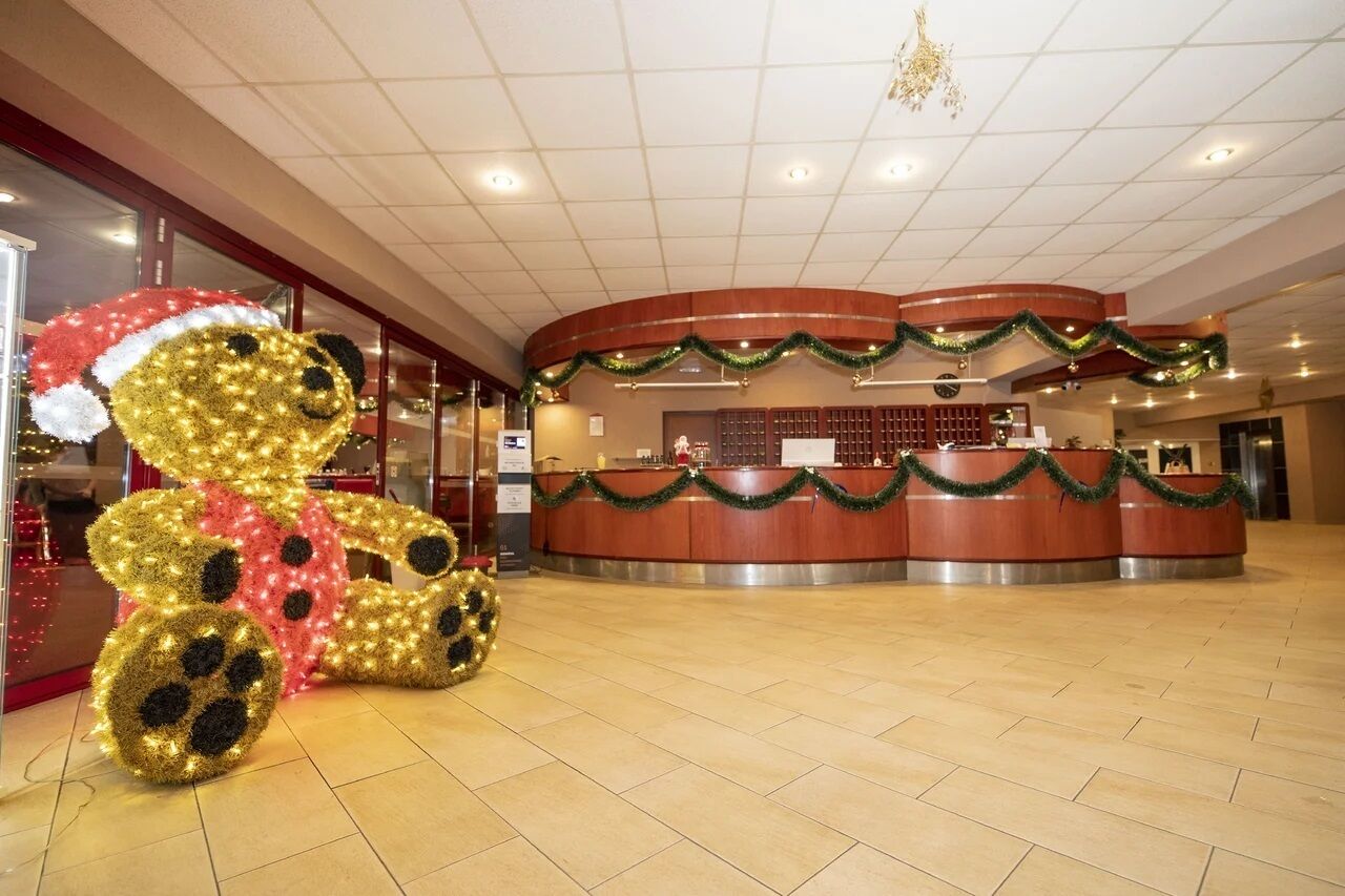 Un espace d’accueil agrémenté d’un grand ours en peluche décoratif, d’un comptoir d’accueil en bois et d’un sol carrelé.
