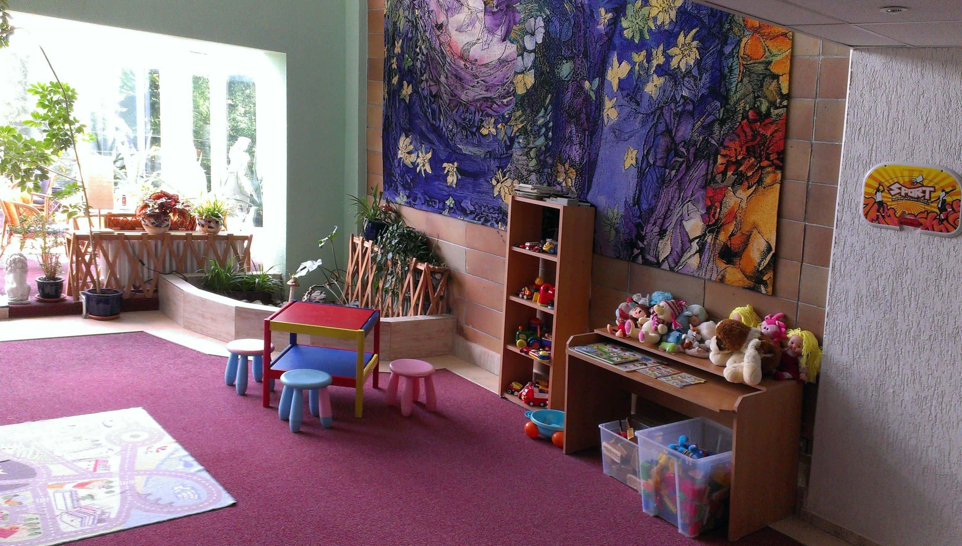 A children's playroom with a colorful mural, a play table, and various toys.