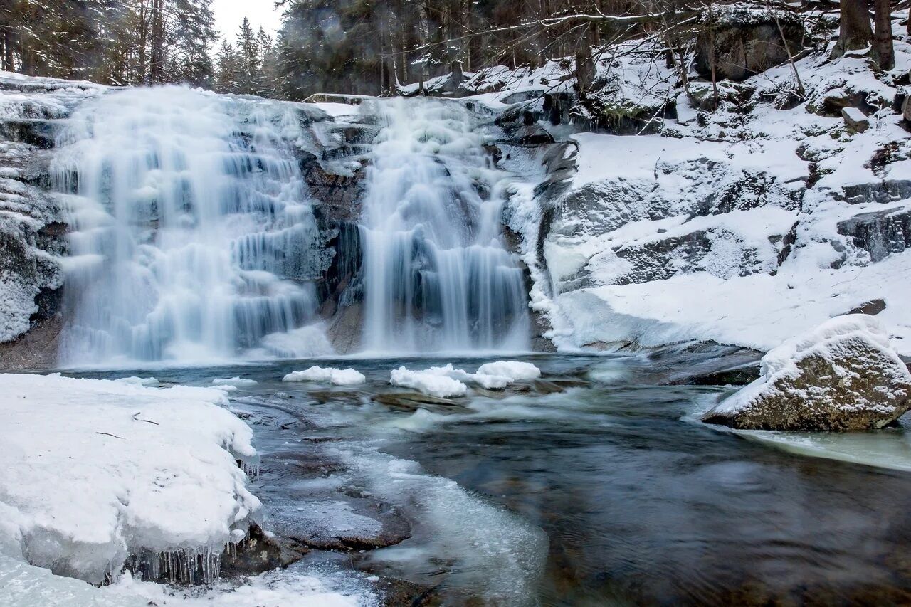 Ein Wasserfall in verschneitem Wald.