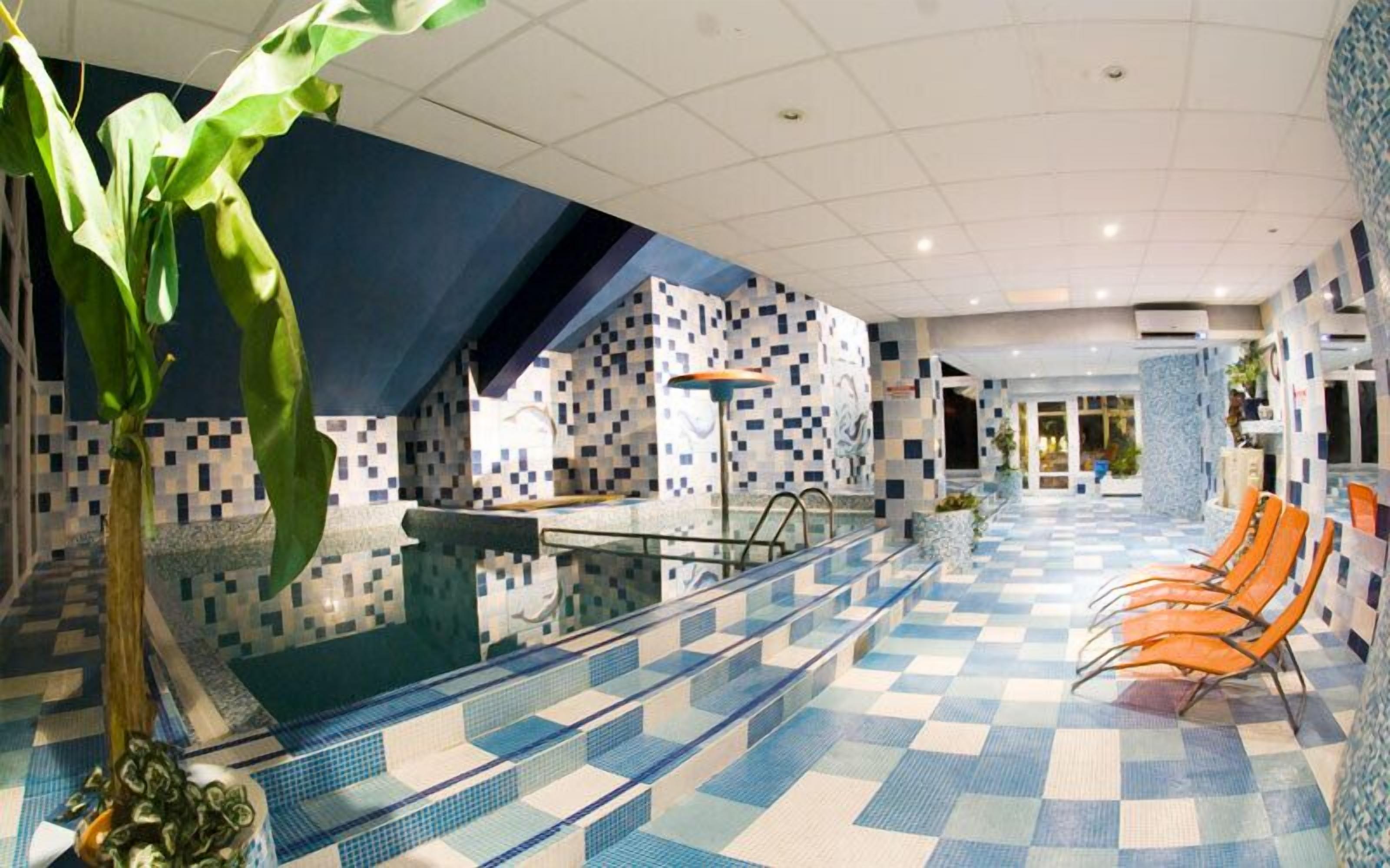 Ein Poolbereich mit Schachbrettboden, einer Glasbarriere und orangefarbenen Stühlen.
