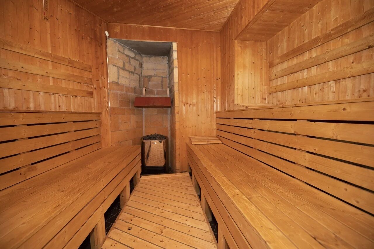 A wooden sauna with benches on either side and a stone wall in the center.