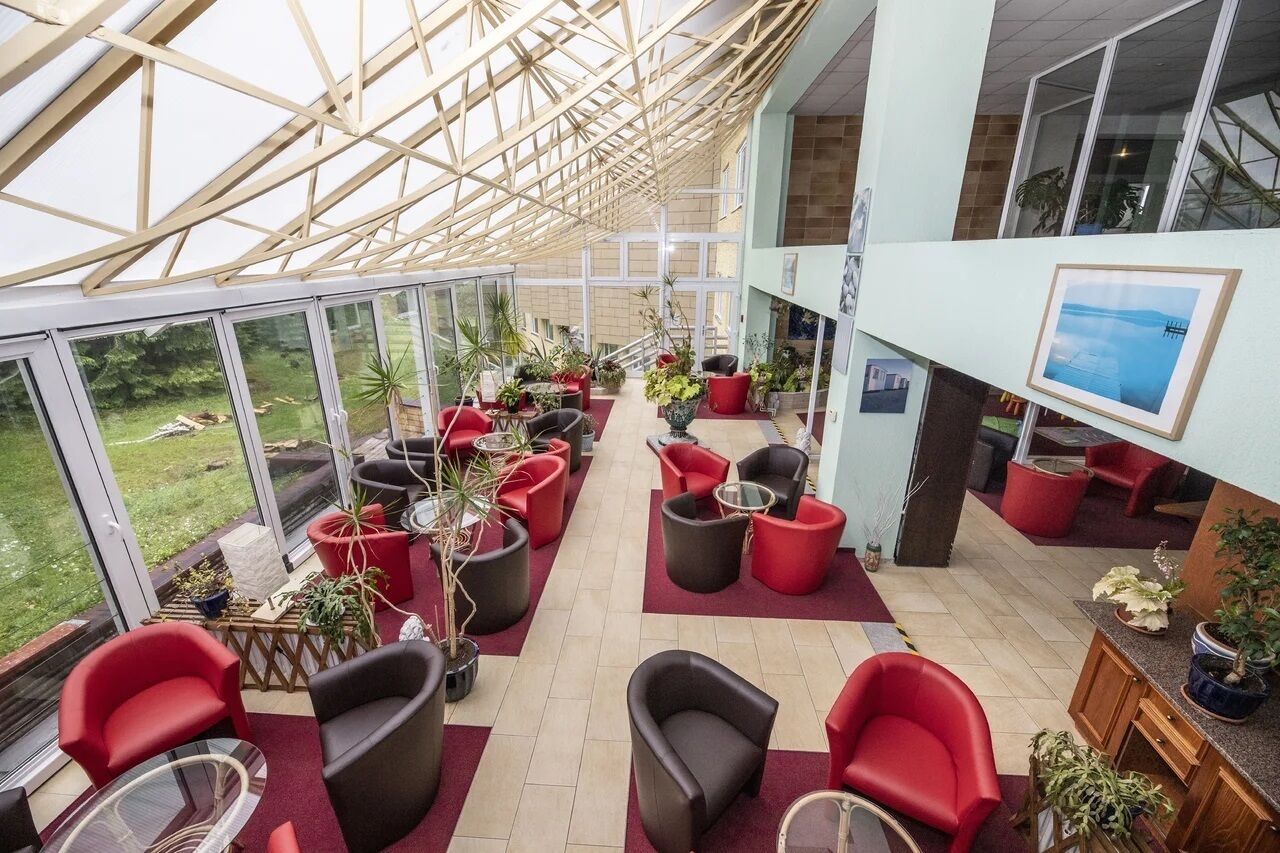 A spacious indoor area with a glass ceiling, red and black chairs, and potted plants.