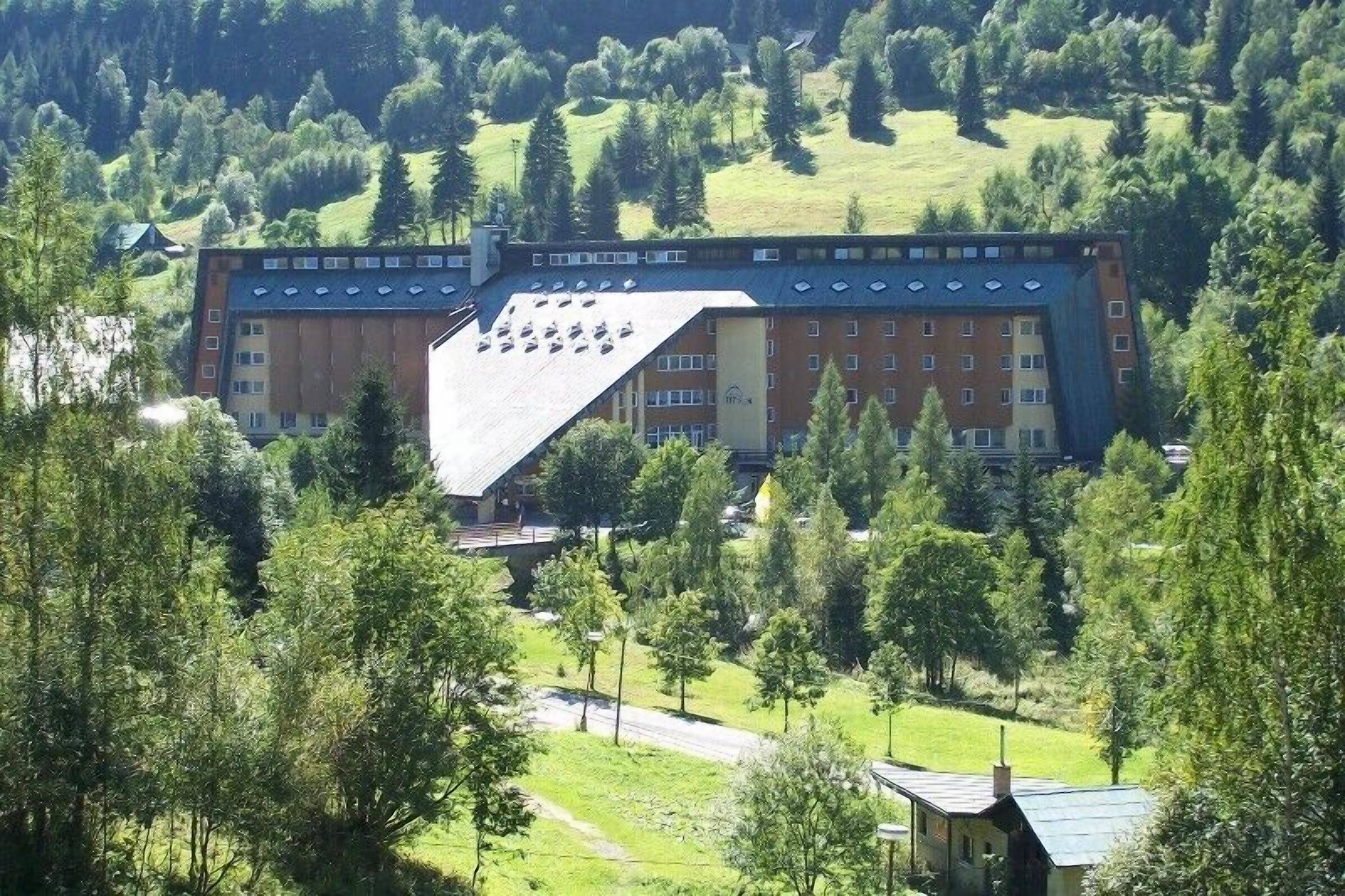 A large building with multiple floors, surrounded by trees and a hilly landscape.