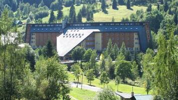 A large building with multiple floors, surrounded by trees and a hilly landscape.