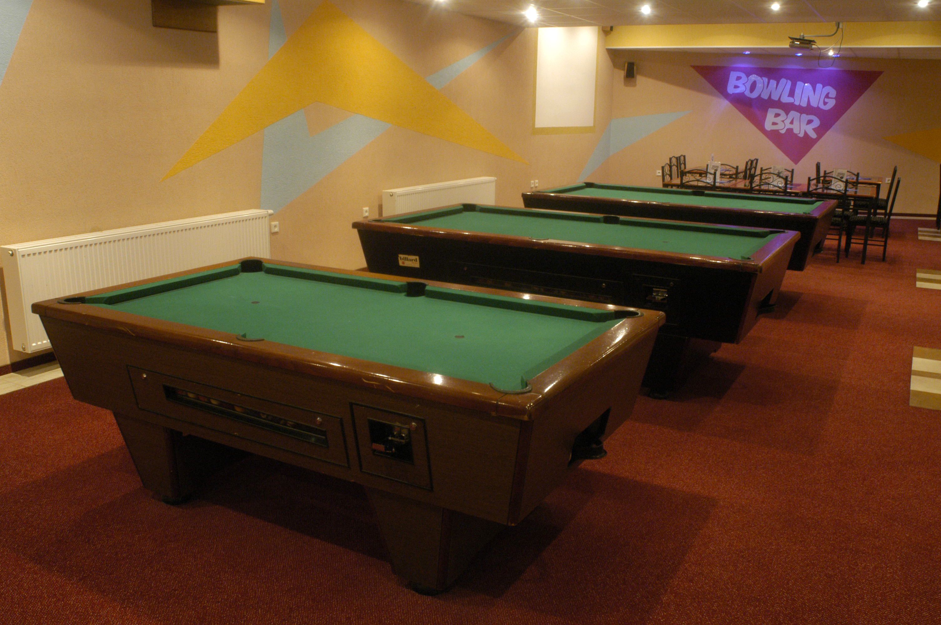 Bolera con varias mesas de billar verdes y una pantalla que muestra 'BOWLING BAR'.
