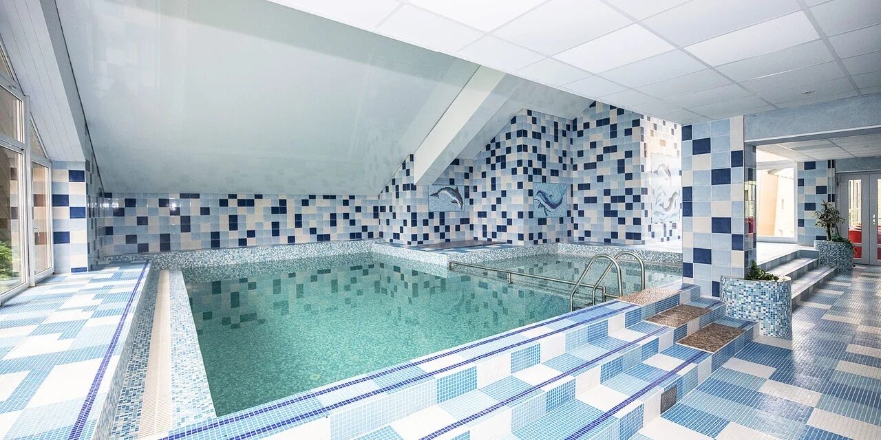 Ein modernes Hallenbad mit Fliesenboden und -wänden, klarem Wasser und einer Glasbarriere.