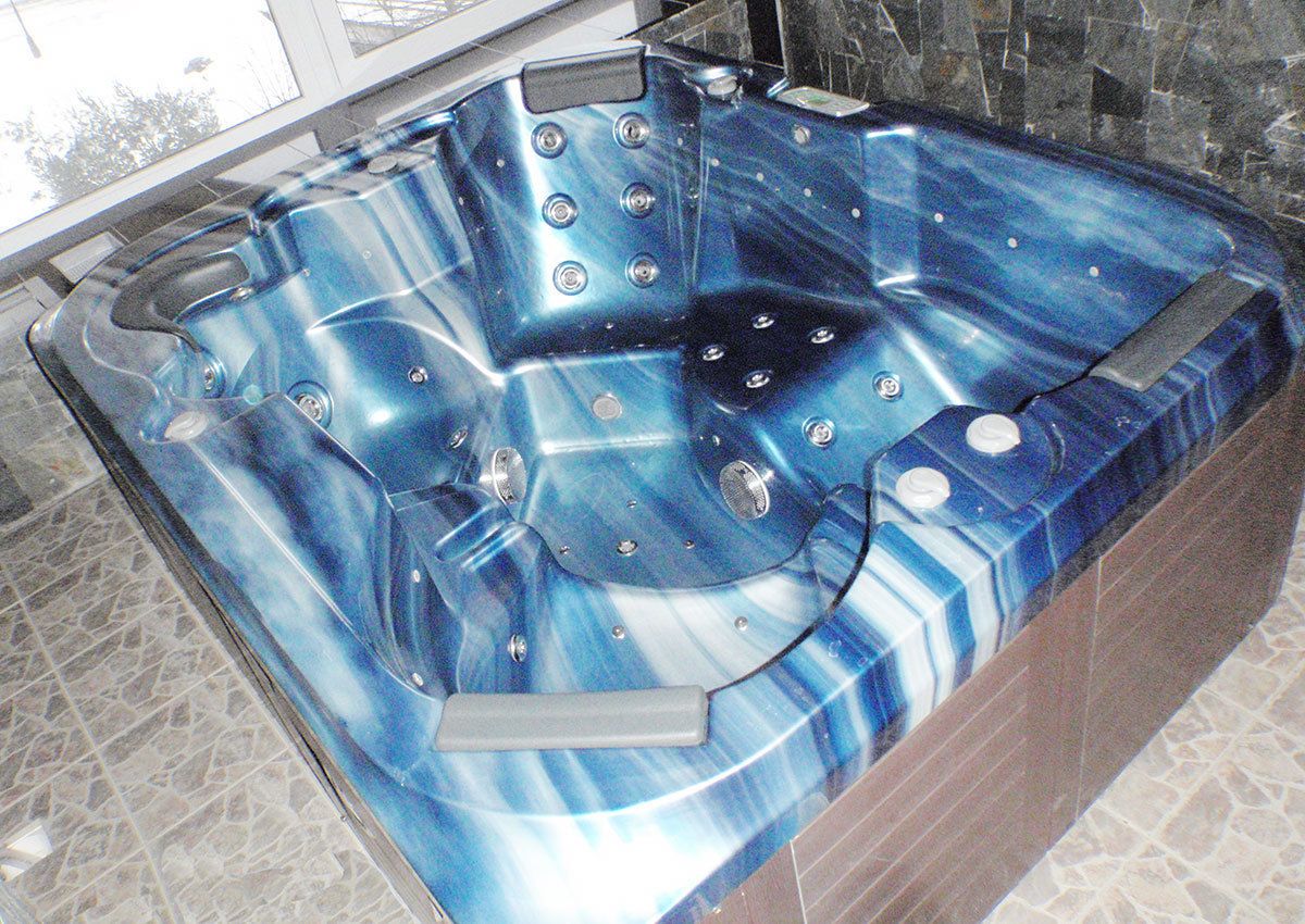 A blue jacuzzi tub with multiple jets, set in a tiled room with a stone wall.