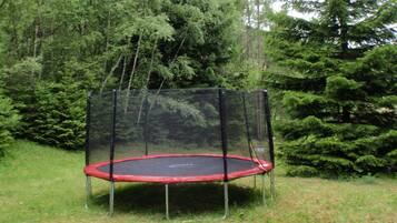 Un trampoline doté d’un filet de sécurité, installé dans un espace herbeux entouré d’arbres.