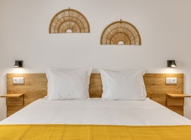 A double bed with white linens, wooden headboard, two wall-mounted lamps, and a yellow throw blanket.