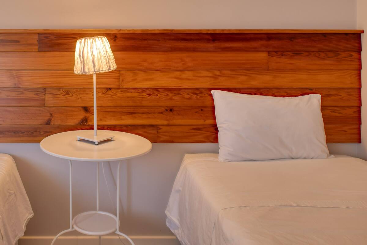 A hotel room with a wooden headboard, a round white side table with a lamp, and a bed with white bedding.